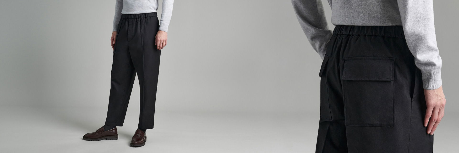 Mann trägt schwarze Hose mit elastischem Bund und Klappentaschen, hellgrauen Pullover und dunkelrote Loafer, stehend vor grauem Hintergrund. Mann trägt schwarze Hose mit elastischem Bund und Klappentaschen, hellgrauen Pullover und dunkelrote Loafer, stehend vor grauem Hintergrund.