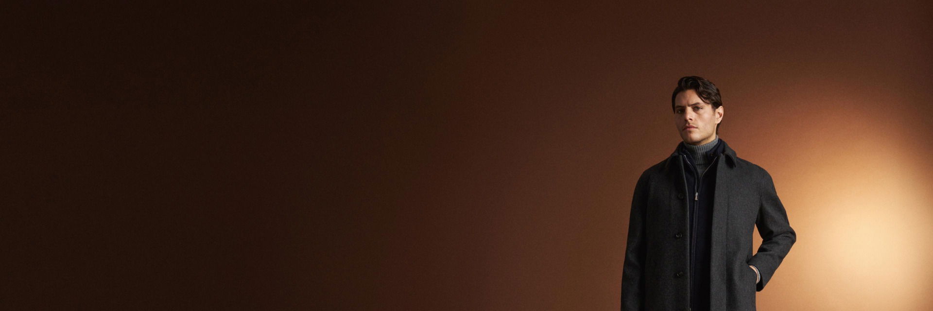 Mann trägt dunkelgrauen Mantel, navy Strickjacke mit Reißverschluss und grauen Rollkragenpullover vor braunem Hintergrund. Mann trägt dunkelgrauen Mantel, navy Strickjacke mit Reißverschluss und grauen Rollkragenpullover vor braunem Hintergrund.