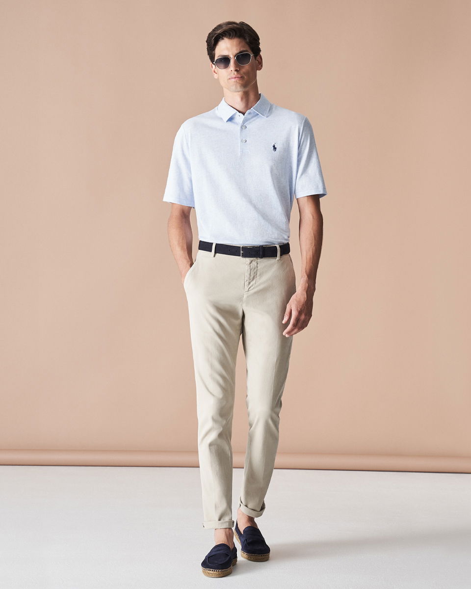 Mann trägt hellblaues Polohemd, beige Hose, schwarzen Gürtel, dunkelblaue Espadrilles und Sonnenbrille vor beigem Hintergrund. Mann trägt hellblaues Polohemd, beige Hose, schwarzen Gürtel, dunkelblaue Espadrilles und Sonnenbrille vor beigem Hintergrund.