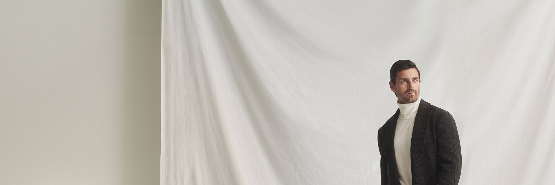 Mann mit braunem Mantel, weißem Rollkragenpullover, beiger Hose und braunen Lederloafers vor weißem Hintergrund. Mann mit braunem Mantel, weißem Rollkragenpullover, beiger Hose und braunen Lederloafers vor weißem Hintergrund.