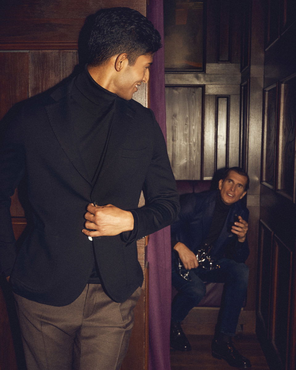 Zwei Männer in dunkler eleganter Kleidung in einem Holz-paneelierten Raum, einer steht im Vordergrund, der andere sitzt im Hintergrund. Zwei Männer in dunkler eleganter Kleidung in einem Holz-paneelierten Raum, einer steht im Vordergrund, der andere sitzt im Hintergrund.