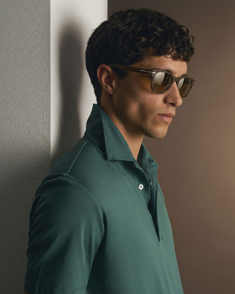 Mann mit kurzen lockigen Haaren, brauner Sonnenbrille und dunkelgrünem Poloshirt mit hochgestelltem Kragen, seitlich stehend. Mann mit kurzen lockigen Haaren, brauner Sonnenbrille und dunkelgrünem Poloshirt mit hochgestelltem Kragen, seitlich stehend.