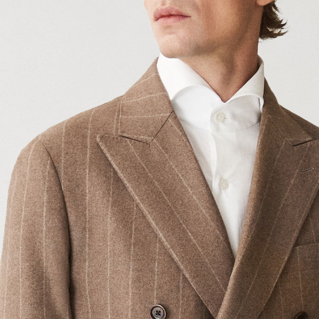 Mann mit braunem, fein gestreiftem Sakko und weißem Hemd, Kopf leicht seitlich, Nahaufnahme Oberkörper.