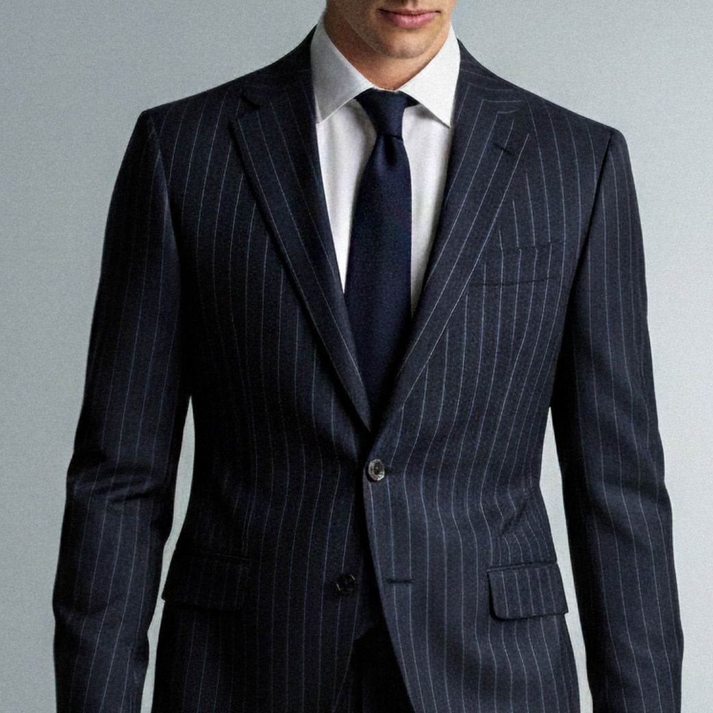Mann trägt dunkelblauen Nadelstreifenanzug mit weißem Hemd und dunkelblauer Krawatte, Oberkörper frontal sichtbar.
