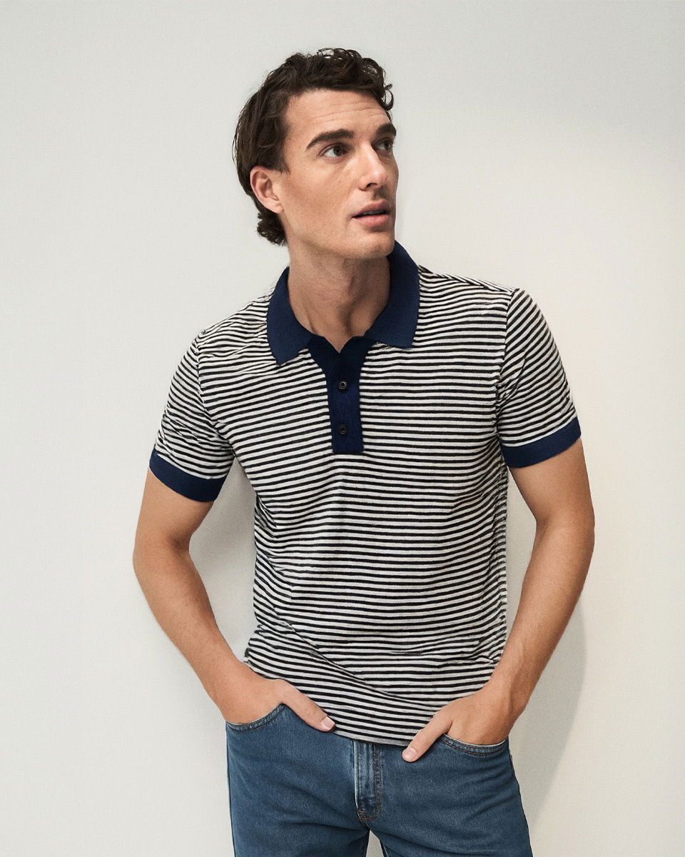 Mann mit kurzen braunen Haaren trägt blau-weiß gestreiftes Strickpoloshirt mit dunkelblauem Kragen und blaue Jeans, schaut seitlich.