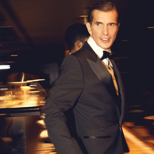 Mann in schwarzem Smoking mit weißem Hemd und schwarzer Fliege steht in elegant beleuchtetem Raum, Blick seitlich. Mann in schwarzem Smoking mit weißem Hemd und schwarzer Fliege steht in elegant beleuchtetem Raum, Blick seitlich.