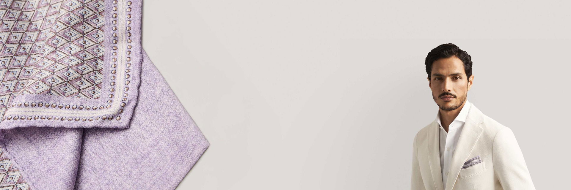 Herr mit weißem Anzug, weißem Hemd und lilafarbenem Einstecktuch mit Muster, vor hellem Hintergrund. Herr mit weißem Anzug, weißem Hemd und lilafarbenem Einstecktuch mit Muster, vor hellem Hintergrund.