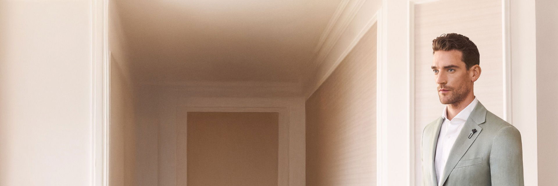 Mann mit weißem Hemd und mintgrünem Sakko steht in elegantem, hell eingerichteten Hotelzimmer vor Fenster. Mann mit weißem Hemd und mintgrünem Sakko steht in elegantem, hell eingerichteten Hotelzimmer vor Fenster.