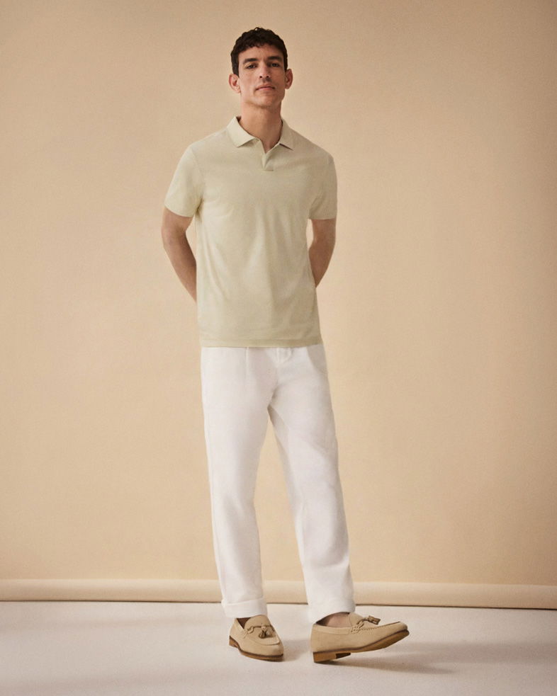 Mann steht vor beigem Hintergrund, trägt hellgrünes Poloshirt, weiße Hose und beige Tassel-Loafer-Schuhe.