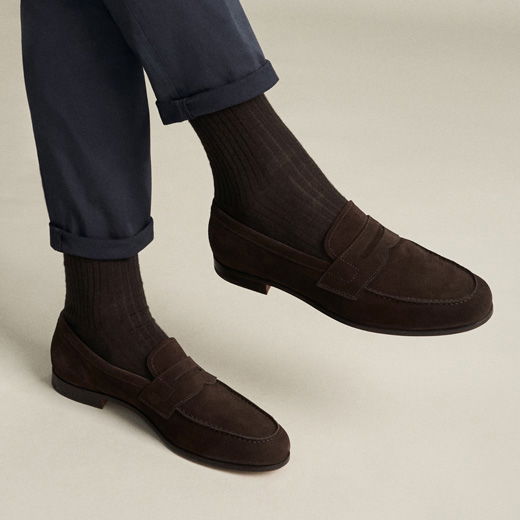 Braune Herrenloafer aus Wildleder mit braunen Rippstrümpfen und navyblauer Hose mit Krempelung. Braune Herrenloafer aus Wildleder mit braunen Rippstrümpfen und navyblauer Hose mit Krempelung.