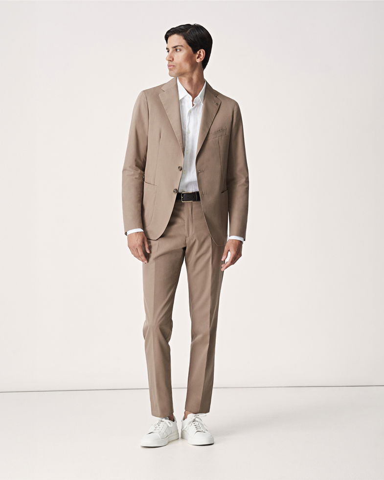 Stehender Herr in einem beigen Anzug mit weißem Hemd und weißen Sneakern Stehender Herr in einem beigen Anzug mit weißem Hemd und weißen Sneakern