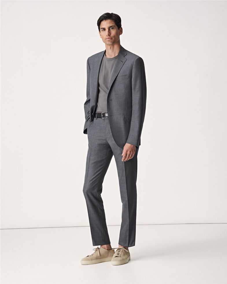 Mann trägt grauen Anzug mit grauem Rundhals-T-Shirt, schwarzen Gürtel und beige Sneaker vor hellem Hintergrund. Mann trägt grauen Anzug mit grauem Rundhals-T-Shirt, schwarzen Gürtel und beige Sneaker vor hellem Hintergrund.