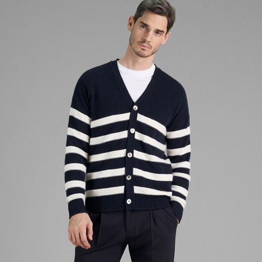 Mann trägt navy-weißen gestreiften Cardigan mit weißen Knöpfen und weißem T-Shirt, steht vor grauem Hintergrund. Mann trägt navy-weißen gestreiften Cardigan mit weißen Knöpfen und weißem T-Shirt, steht vor grauem Hintergrund.