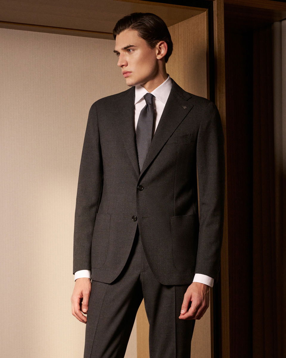 Mann im eleganten schwarzen Anzug mit weißem Hemd und gemusterter Krawatte, stehend vor beigem Hintergrund. Mann im eleganten schwarzen Anzug mit weißem Hemd und gemusterter Krawatte, stehend vor beigem Hintergrund.