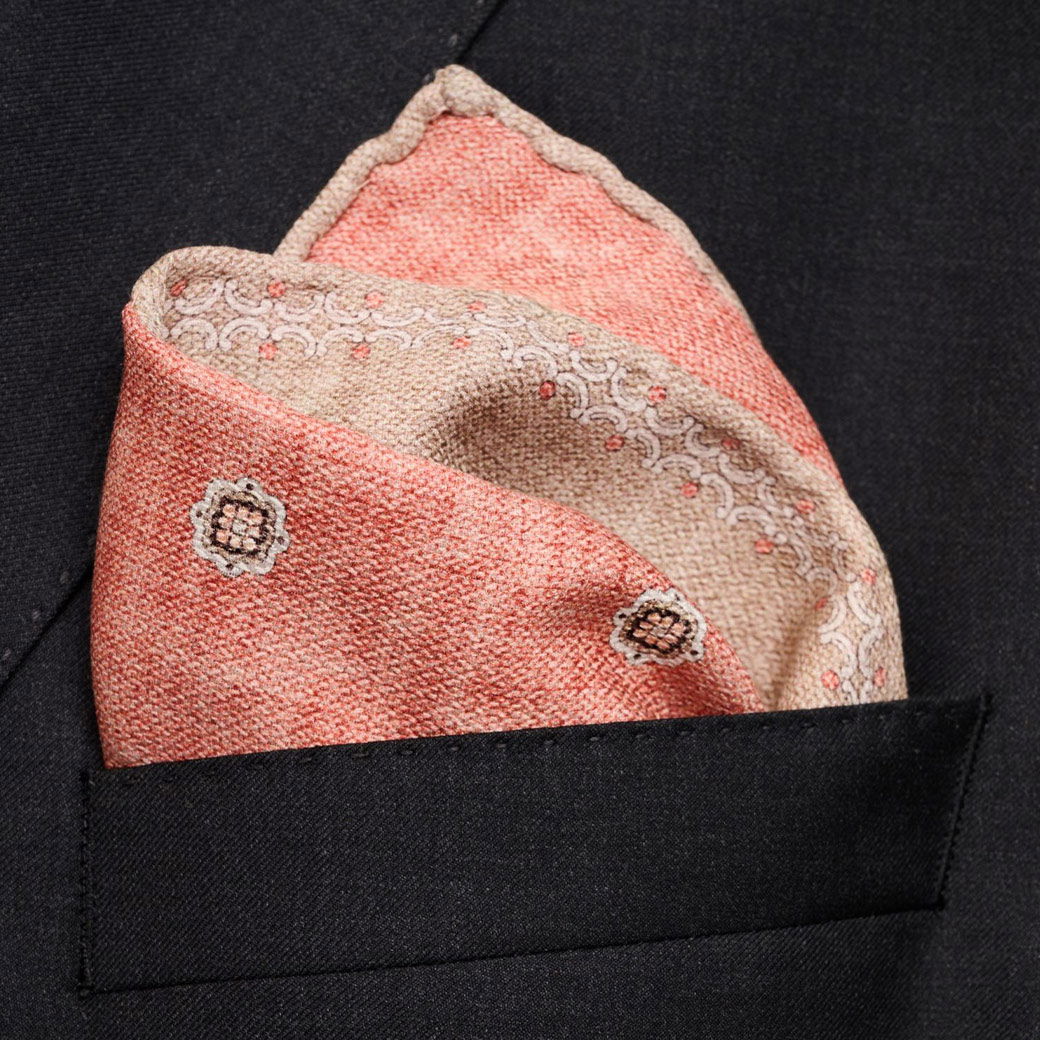 Oranges und beiges floral gemustertes Einstecktuch, kunstvoll in die Brusttasche eines schwarzen Sakkos gefaltet.