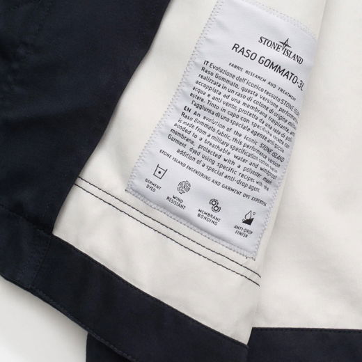 Innenansicht einer Herrenjacke mit weißem Innenfutter, schwarzem Rand und Stoffetikett von Stone Island.