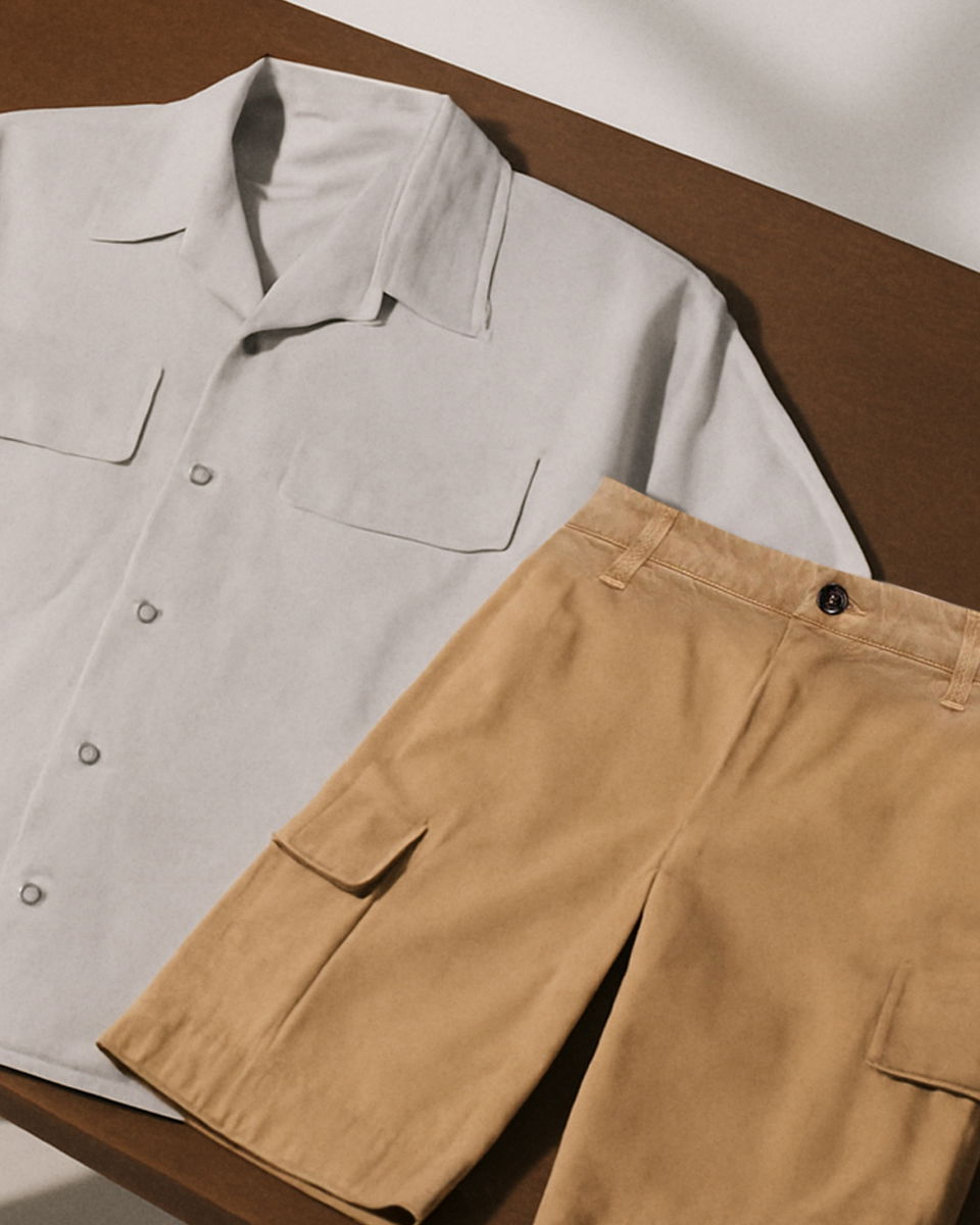 Hellgraues Kurzarmhemd mit Taschen und hellbraune Cargoshorts mit Knopf auf braunem Tisch liegend. Hellgraues Kurzarmhemd mit Taschen und hellbraune Cargoshorts mit Knopf auf braunem Tisch liegend.