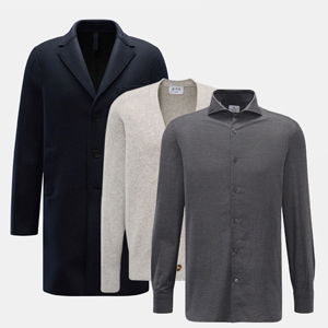 Navyblauer Mantel, hellgrauer Cardigan und dunkelgraues Hemd nebeneinander auf weißem Hintergrund. Navyblauer Mantel, hellgrauer Cardigan und dunkelgraues Hemd nebeneinander auf weißem Hintergrund.
