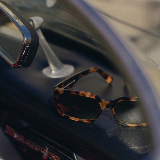 Sonnenbrille mit braun-schwarzem Muster liegt auf dem Armaturenbrett eines Autos, Rückspiegel sichtbar.