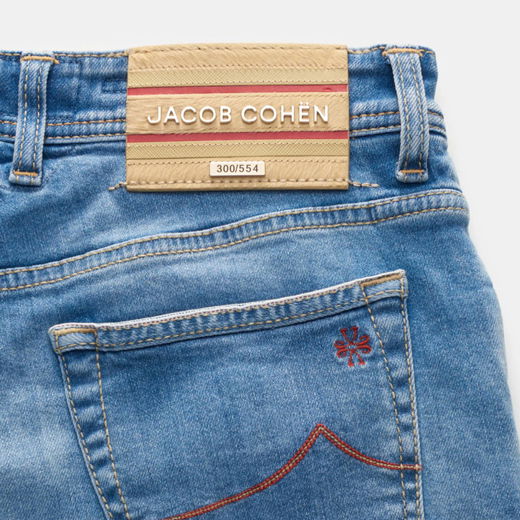 Nahaufnahme der Rückseite einer blauen Selvedge Denim Jeans mit hellbraunem Lederpatch „Jacob Cohën“ und roter Ziernaht am Taschenrand.