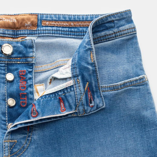 Nahaufnahme des Bundes einer blauen Selvedge-Denim-Jeans für Herren mit sichtbarer Knopfleiste und roten Knopflöchern.