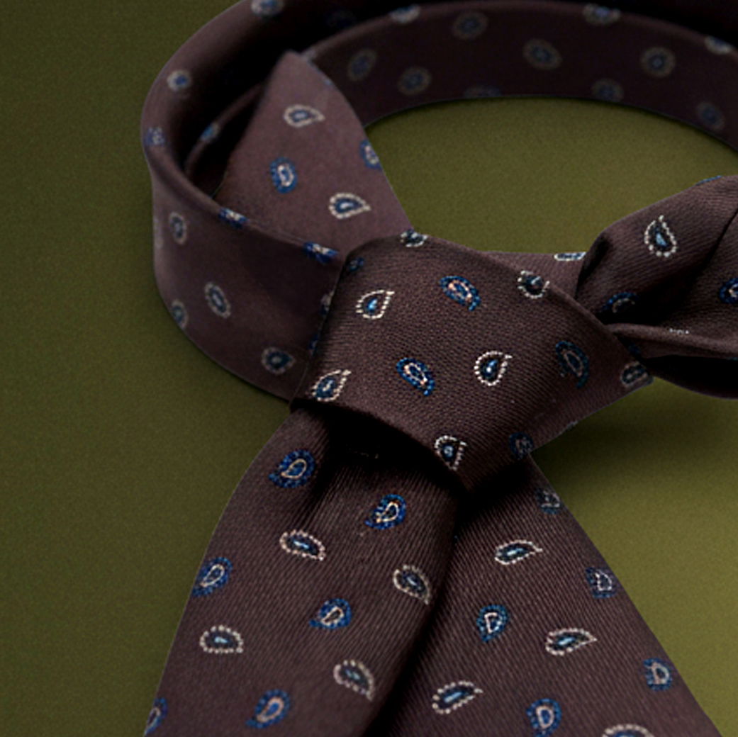 Nahaufnahme einer dunkelbraunen Krawatte mit blau-weißem Paisley-Muster auf grünem Hintergrund, gebunden.