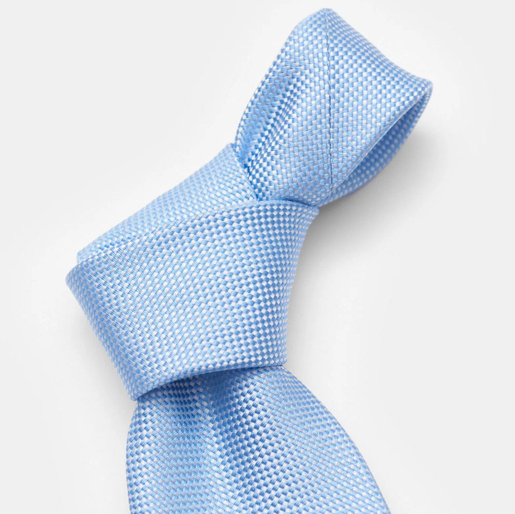 Nahaufnahme einer hellblauen Seidenkrawatte mit feinem, kariertem Webmuster und elegant gebundenem Knoten. Nahaufnahme einer hellblauen Seidenkrawatte mit feinem, kariertem Webmuster und elegant gebundenem Knoten.