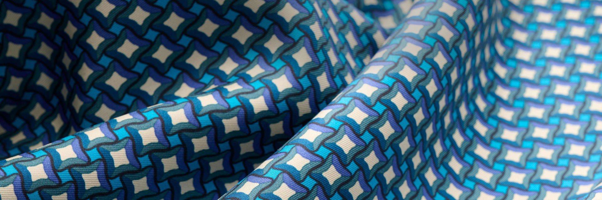 Nahaufnahme eines Seidenstoffes mit weiß-blau-lila geometrischem Muster und feiner Struktur in Falten gelegt Nahaufnahme eines Seidenstoffes mit weiß-blau-lila geometrischem Muster und feiner Struktur in Falten gelegt