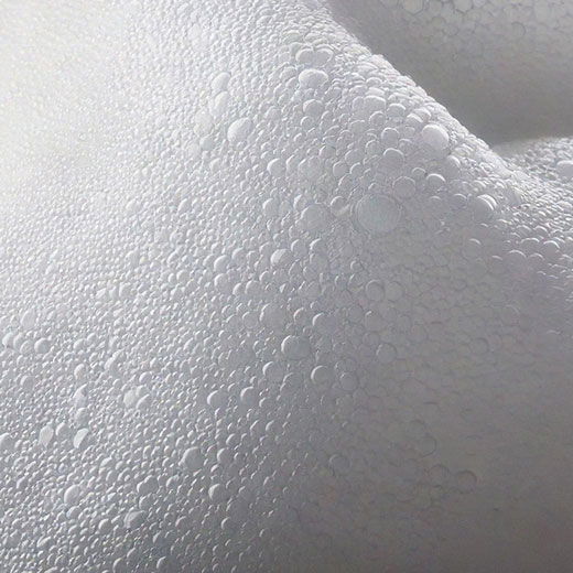 Nahaufnahme von weißem Schaum mit vielen kleinen, runden Luftbläschen unterschiedlicher Größe auf einer glatten Oberfläche.