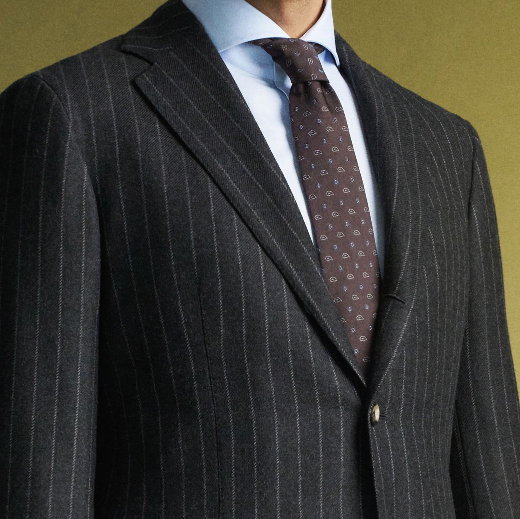 Herrenoberkörper mit dunkelgrauem Nadelstreifen-Sakko, hellblauem Hemd und dunkelroter Krawatte mit Muster vor grünem Hintergrund.