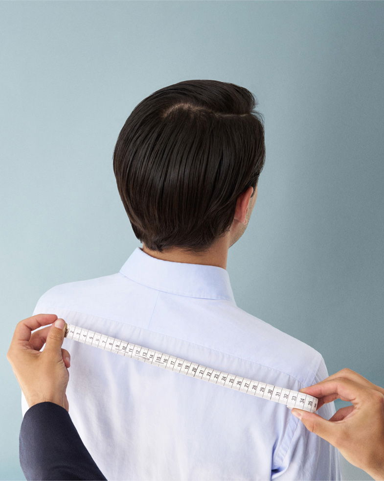 Person wird von hinten beim Maßnehmen für ein maßgeschneidertes Hemd mit einem Maßband am Rücken fotografiert.