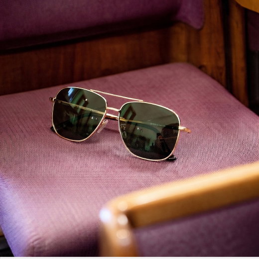 Piloten-Sonnenbrille mit goldfarbenem Metallgestell und dunkel getönten Gläsern liegt auf violettem Stuhlpolster.