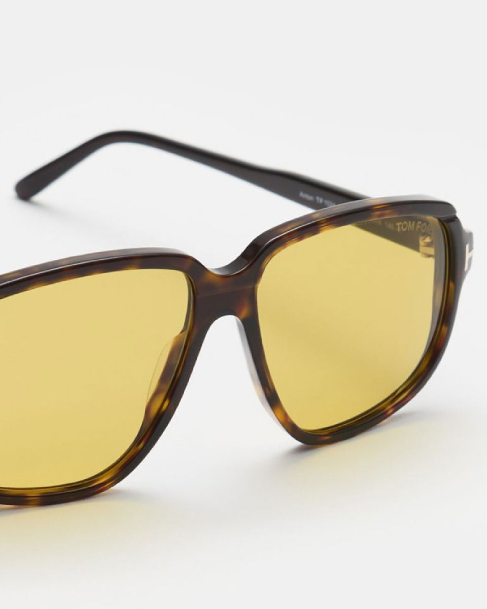 Rechteckige Sonnenbrille mit braunem, gemustertem Schildpatt-Rahmen und gelb getönten Gläsern auf weißem Hintergrund.