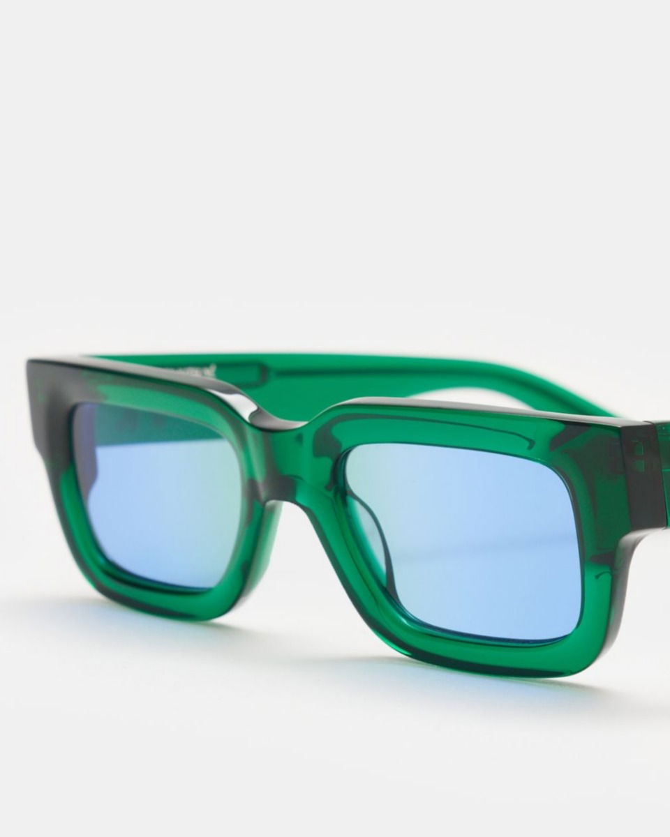 Rechteckige Sonnenbrille mit transparent grünem Rahmen und breiten hellblauen Gläsern, frontal auf weißem Hintergrund.