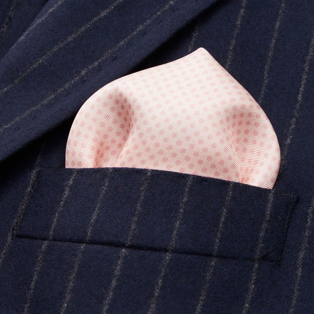 Rosa Einstecktuch mit feinem Muster, gefaltet in der Brusttasche eines dunkelblauen Herren-Sakkos mit grauen Nadelstreifen.