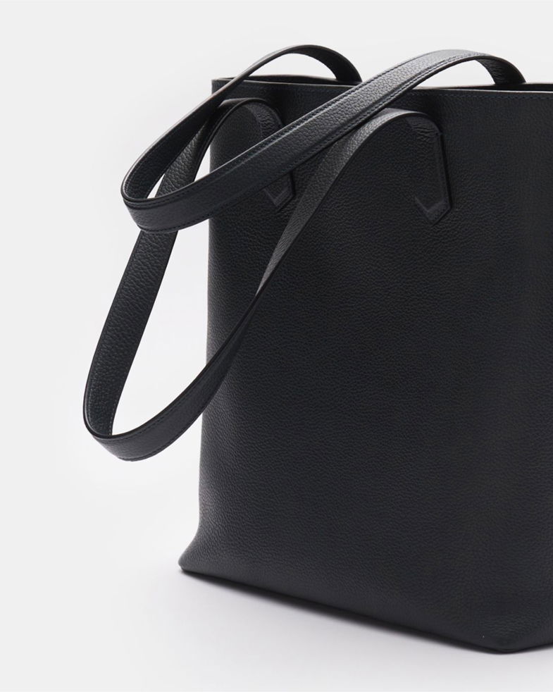 Schwarze Leder Tote Bag mit großer Seitenansicht, schlichter Struktur und zwei langen Tragegriffen, vor hellem Hintergrund. Schwarze Leder Tote Bag mit großer Seitenansicht, schlichter Struktur und zwei langen Tragegriffen, vor hellem Hintergrund.