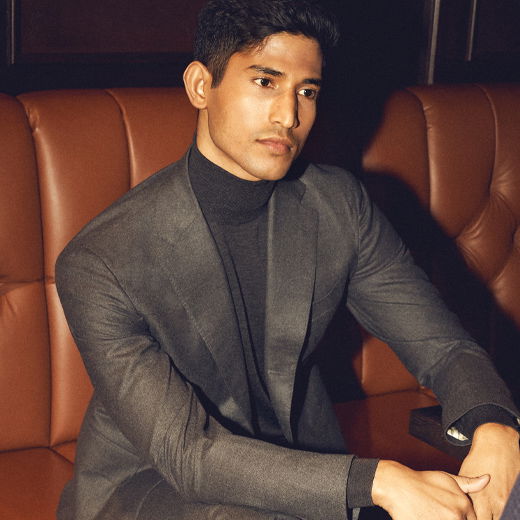 Junger Mann mit grauem Anzugsakko und schwarzem Rollkragenpullover sitzt nachdenklich in braunem Ledersitz im Restaurant. Junger Mann mit grauem Anzugsakko und schwarzem Rollkragenpullover sitzt nachdenklich in braunem Ledersitz im Restaurant.