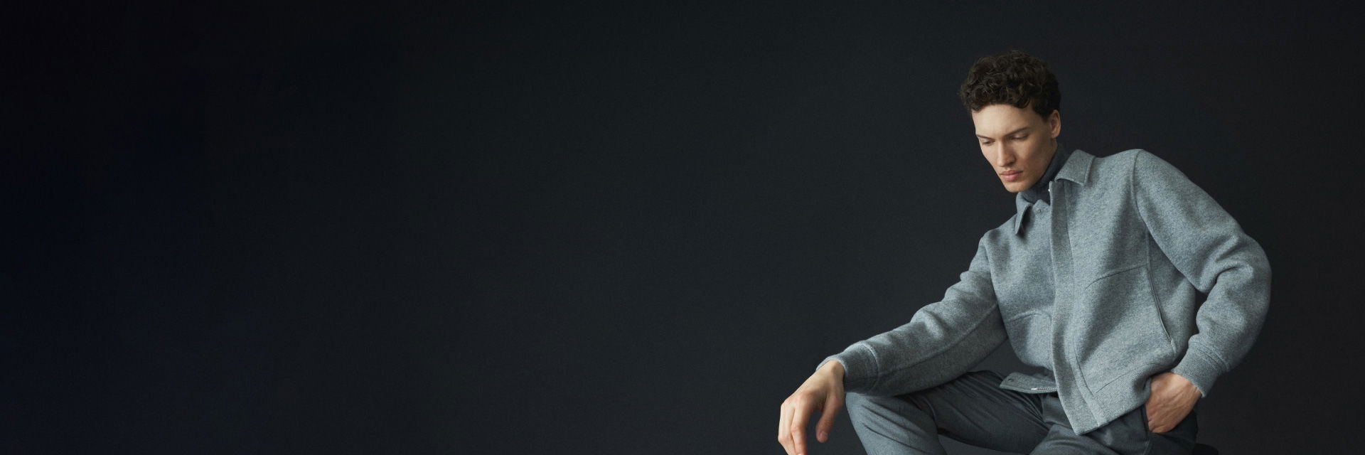 Sitzender Mann in grauer Hose, grauem Rollkragenpullover und grauem meliertem Overshirt vor dunklem Hintergrund. Sitzender Mann in grauer Hose, grauem Rollkragenpullover und grauem meliertem Overshirt vor dunklem Hintergrund.