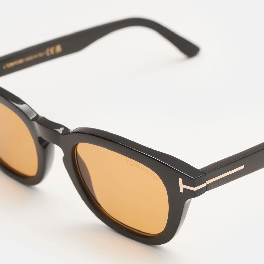 Schwarze Herren-Sonnenbrille mit rechteckigem Rahmen, goldfarbenem Detail und gelb getönten Gläsern, von Tom Ford.