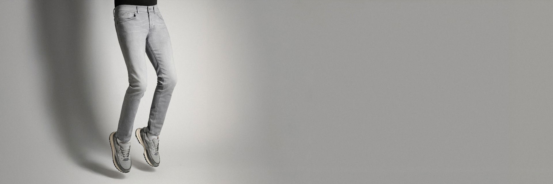 Springender Mann von der Hüfte abwärts mit hellgrauer Jeans und grauen Sneakern vor hellgrauem Hintergrund. Springender Mann von der Hüfte abwärts mit hellgrauer Jeans und grauen Sneakern vor hellgrauem Hintergrund.