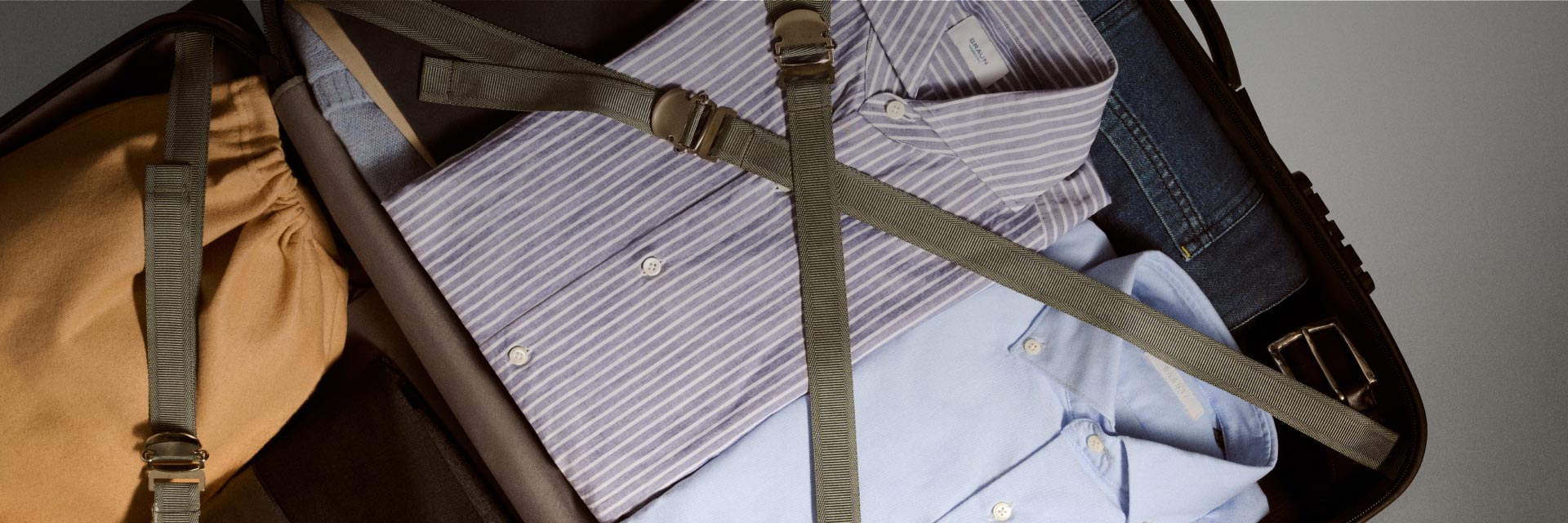 Von oben fotografierter geöffneter Koffer mit zwei Hemden, Jeans, Gürtel und Schuhbeutel, alles ordentlich verstaut. Von oben fotografierter geöffneter Koffer mit zwei Hemden, Jeans, Gürtel und Schuhbeutel, alles ordentlich verstaut.