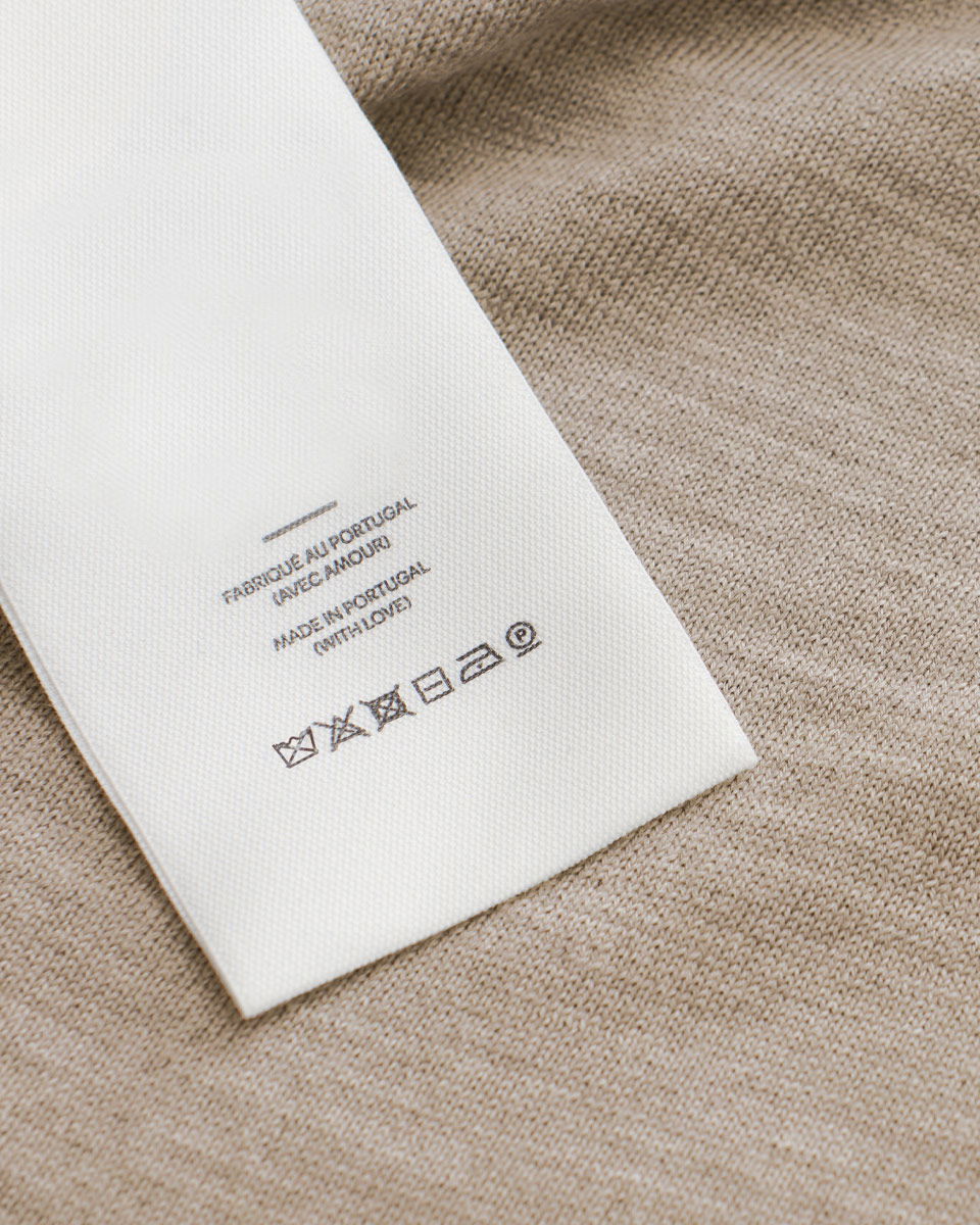 Waschlabel mit Pflegehinweisen und Text 'Made in Portugal' auf beigem Cashmerestoff, mit Waschsymbolen unten.