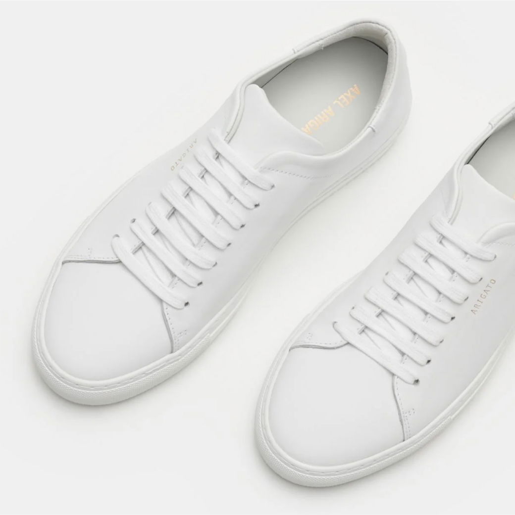 Weiße Herren-Sneaker aus glattem Leder mit weißen Schnürsenkeln, seitlicher Markenaufdruck und minimalistischer Optik, Vogelperspektive. Weiße Herren-Sneaker aus glattem Leder mit weißen Schnürsenkeln, seitlicher Markenaufdruck und minimalistischer Optik, Vogelperspektive.