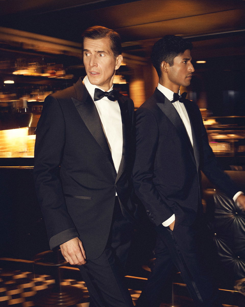 Zwei Herren in schwarzen Smokings mit weißen Hemden und schwarzen Fliegen in elegantem, festlichem Ambiente. Zwei Herren in schwarzen Smokings mit weißen Hemden und schwarzen Fliegen in elegantem, festlichem Ambiente.