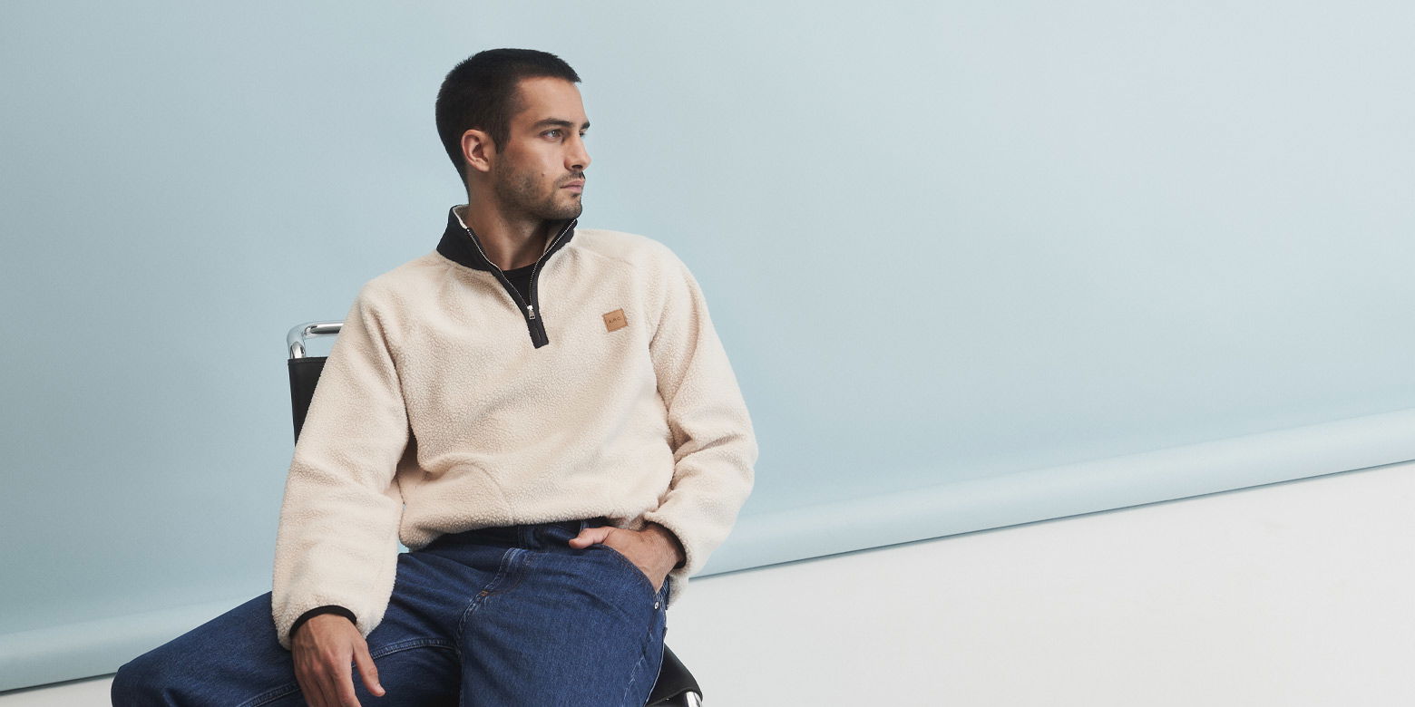 Sitzender Herr mit cremefarbenem Troyer aus Fleece zur blauen Jeans