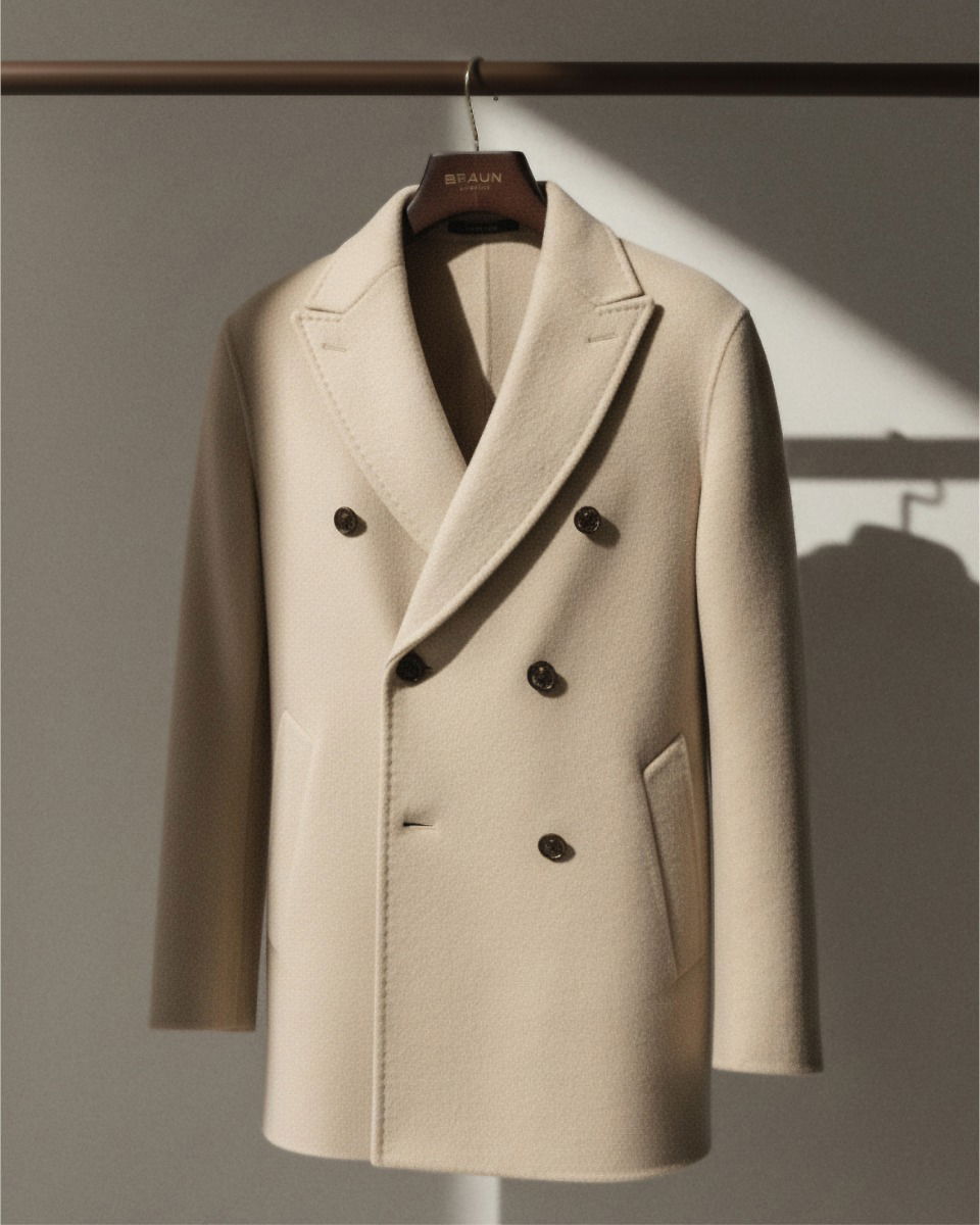 Beiger, doppelt geknöpfter Wollmantel mit Reverskragen an einem Holzkleiderbügel vor hellem Hintergrund. Beiger, doppelt geknöpfter Wollmantel mit Reverskragen an einem Holzkleiderbügel vor hellem Hintergrund.