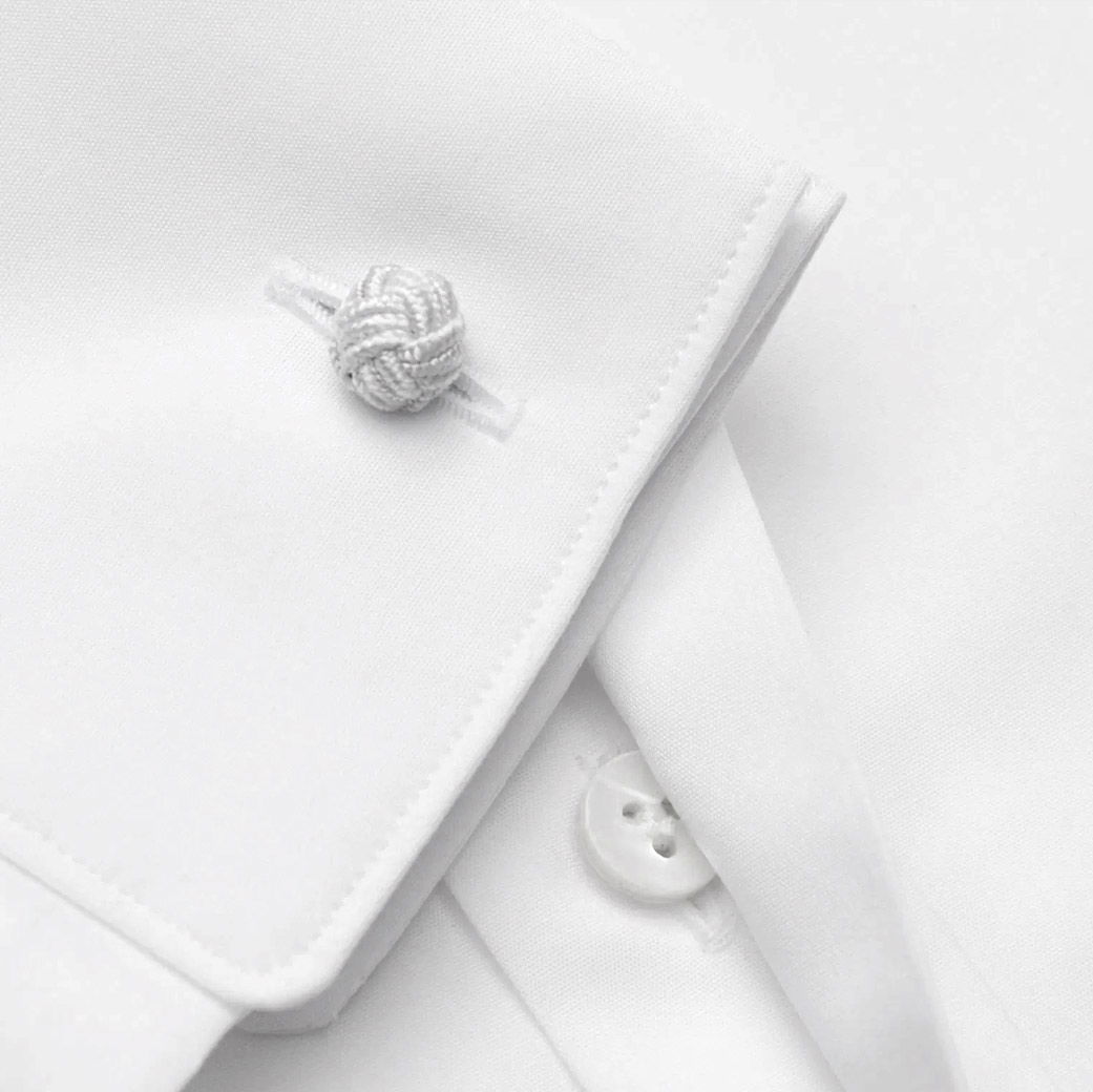 Weiße Umschlagmanschette eines Herrenhemdes mit Knotenmanschettenknopf aus geflochtenem Stoff und sichtbarem weißen Knopf.