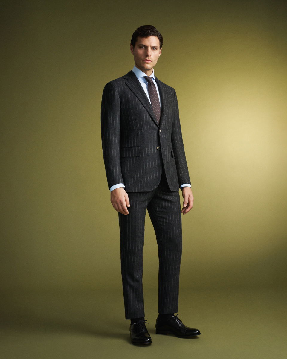 Mann im dunklen Nadelstreifen-Anzug mit weißem Hemd und gemusterter Krawatte vor olivgrünem Hintergrund stehend. Mann im dunklen Nadelstreifen-Anzug mit weißem Hemd und gemusterter Krawatte vor olivgrünem Hintergrund stehend.