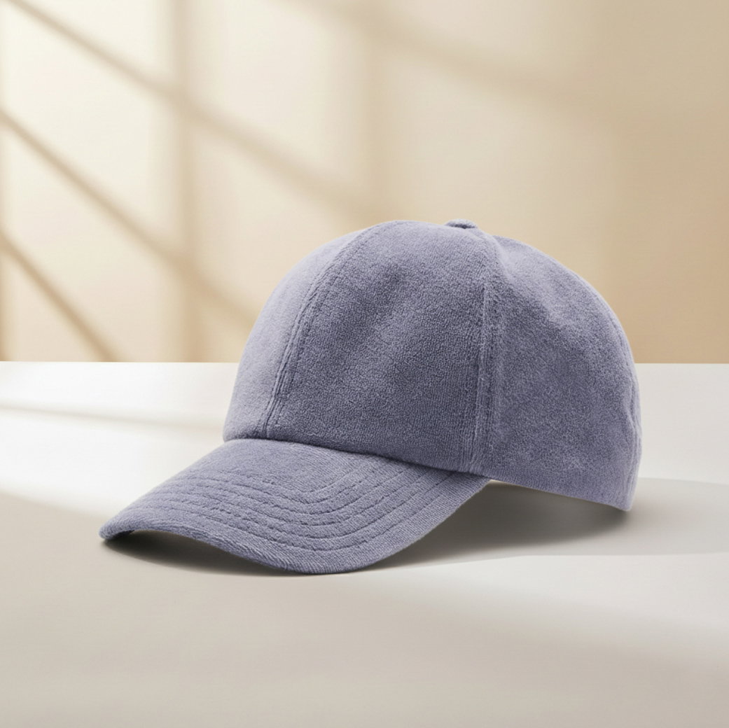 Hellviolette Baseballcap aus weichem, samtartigem Stoff liegt auf weißer Oberfläche vor beigem Hintergrund mit Schatten.