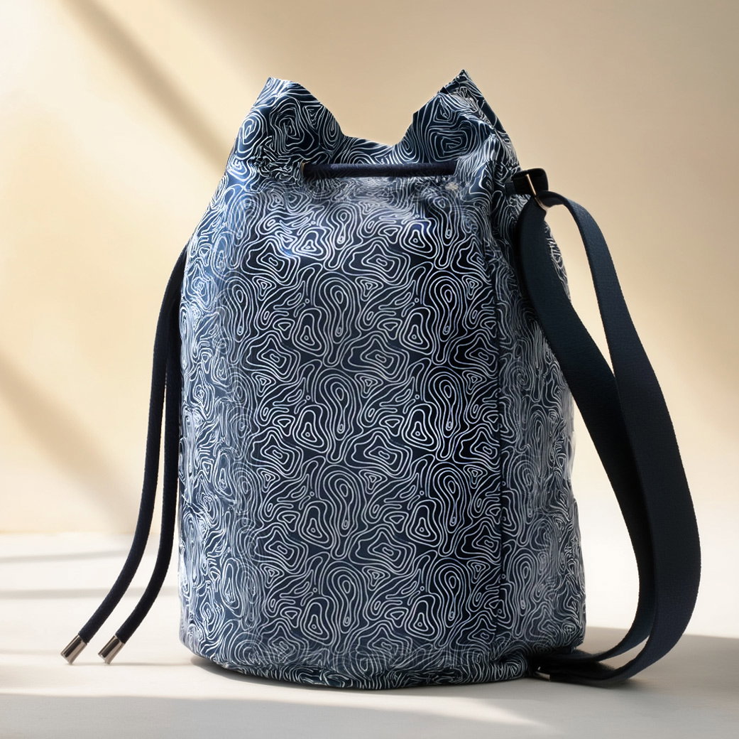 Blau-weiße Tasche mit abstraktem Linienmuster, Kordelzugverschluss und verstellbarem Schulterriemen, vor hellem Hintergrund.